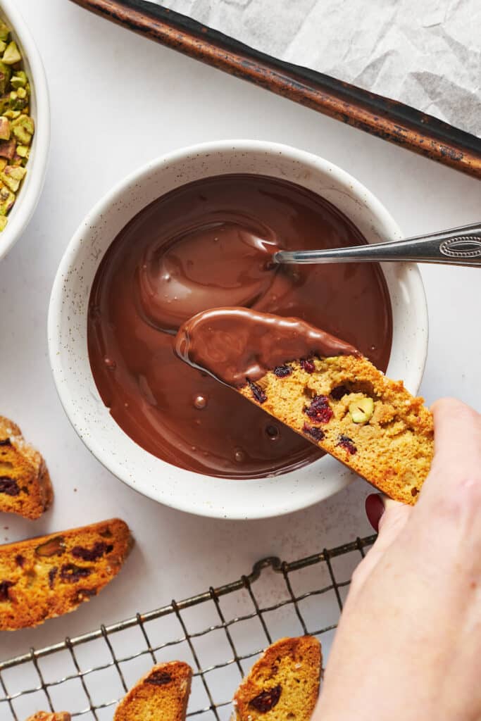 Cranberry orange biscotti being dunked into chocolate.