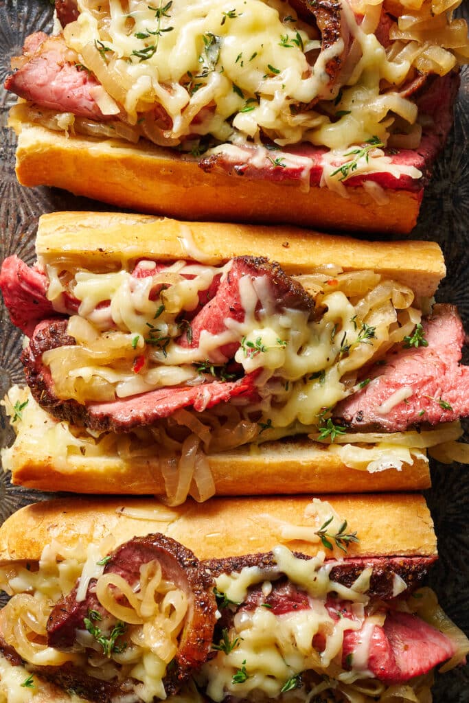 French dip sandwiches with gooey cheese on baking sheet.