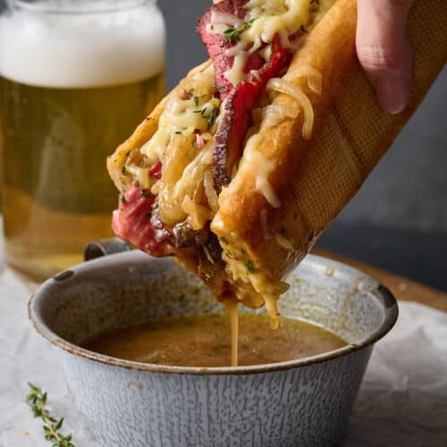 French dip sandwiches being dipped into a side of au jus sauce.