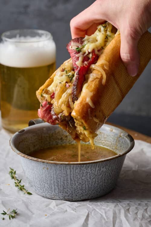 French dip sandwiches being dipped into a side of au jus sauce.