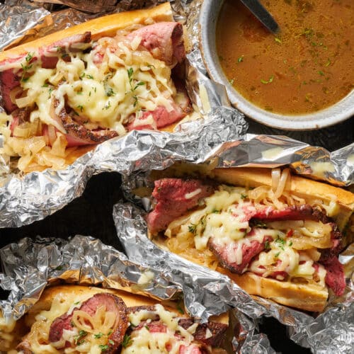 French dip sandwiches wrapped in aluminum foil with au jus on the side.