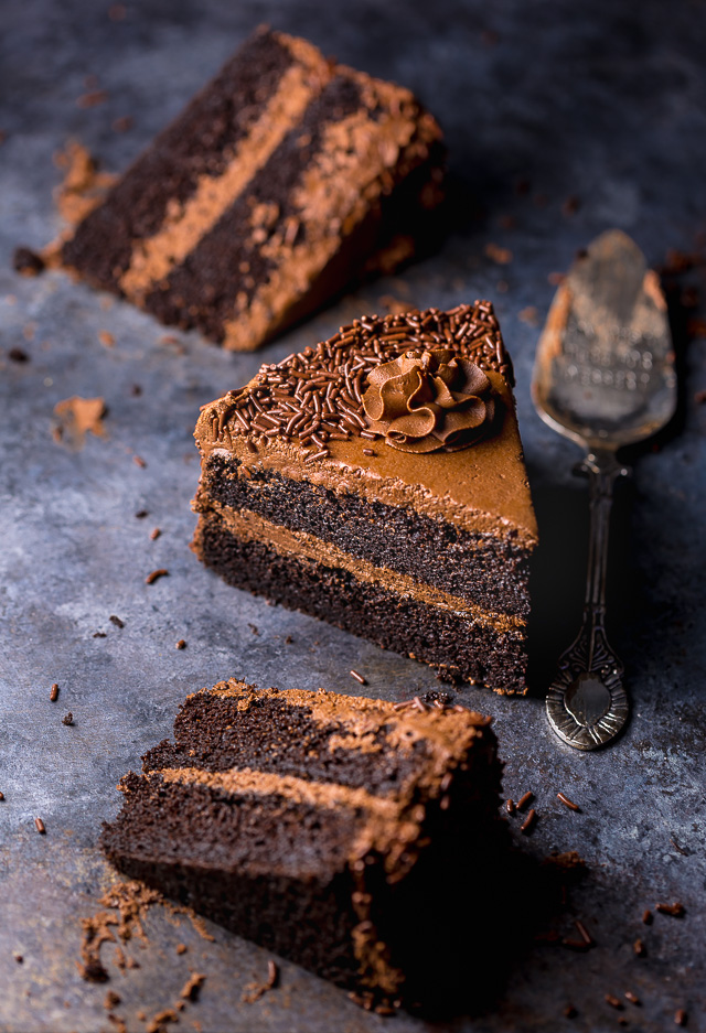 Slices of chocolate cake on a dark table with a cake server.