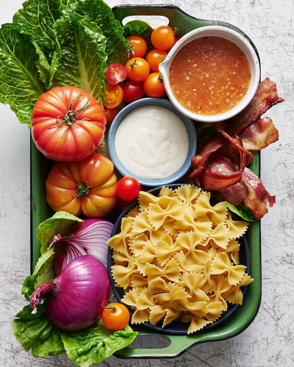 Green metal pan with pasta salad ingredients inside.