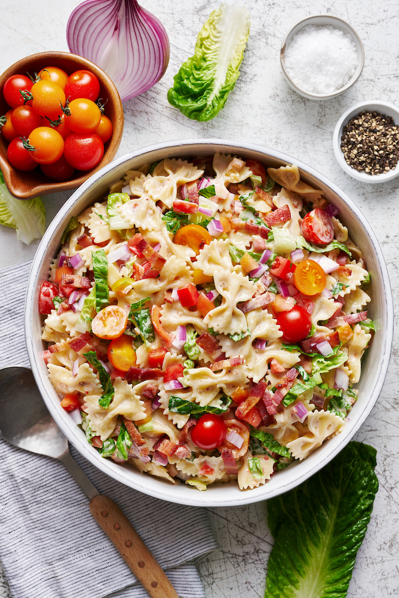 Big bowl of pasta salad tossed in creamy homemade dressing and topped with bacon, lettuce, and tomato.