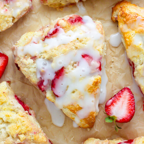 Strawberry scones on brown parchment paper with glaze drizzled on top.