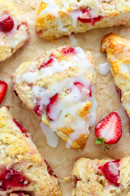 Strawberry scones on brown parchment paper with glaze drizzled on top.