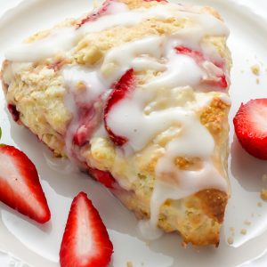 Strawberry scone with creamy glaze on a white plate.