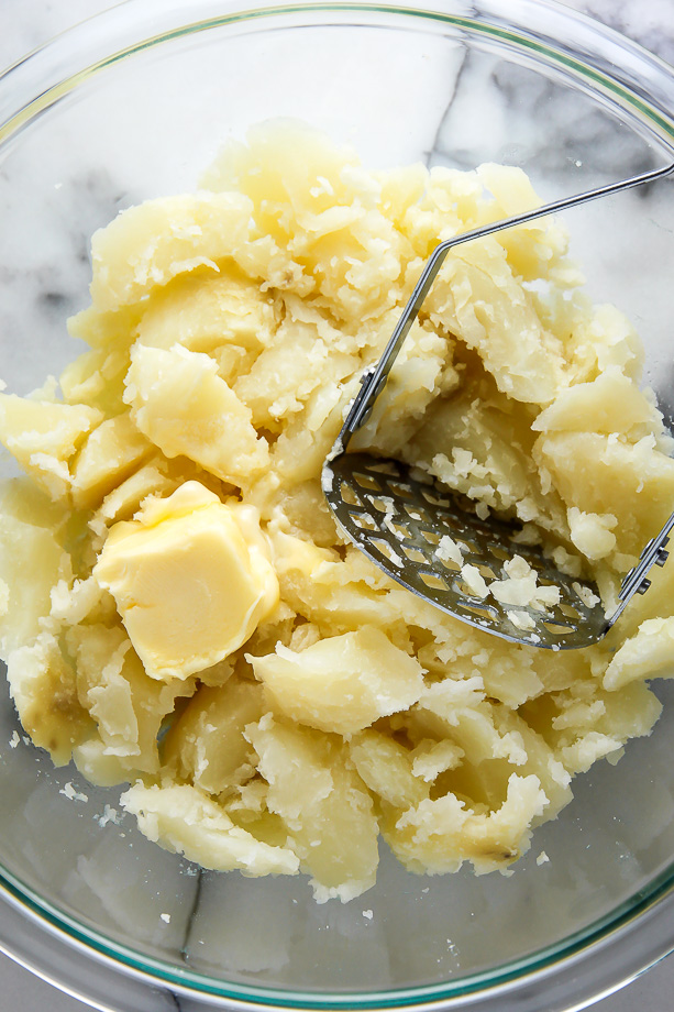 Mashed potatoes with potato masher in a mixing bowl.