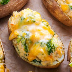 Twice-baked potatoes on parchment paper topped with broccoli and cheese.