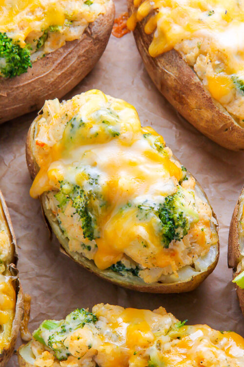 Twice-baked potatoes on parchment paper topped with broccoli and cheese.