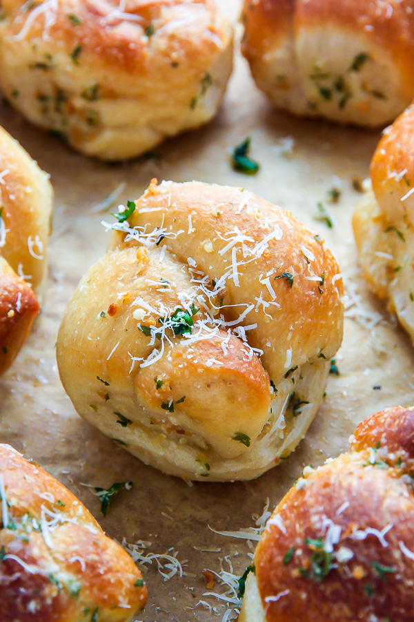 Homemade garlic knots topped with Parmesan cheese on a baking sheet with parchment paper.