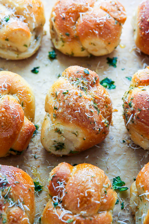 Garlic knots on a baking sheet with parsley, garlic powder, and grated parmesan cheese on top.