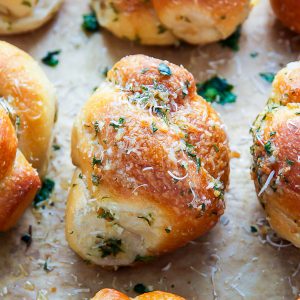Homemade garlic knots on a baking sheet with grated parmesan cheese on top.