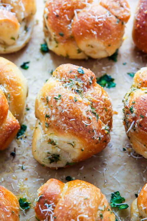 Homemade garlic knots on a baking sheet with grated parmesan cheese on top.