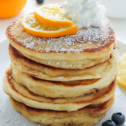 A stack of lemon ricotta pancakes with whipped cream on top.