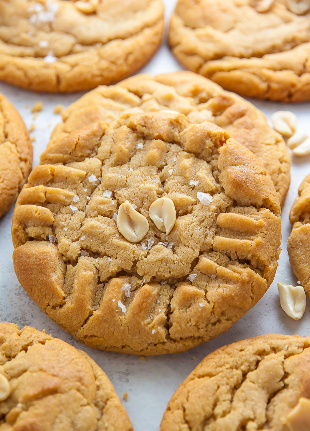 Peanut butter cookies on white parchment paper with peanuts on top.