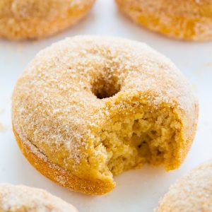 Baked cinnamon sugar donuts with a bite taken out on parchment paper.