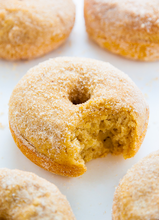 Baked cinnamon sugar donuts with a bite taken out on parchment paper.
