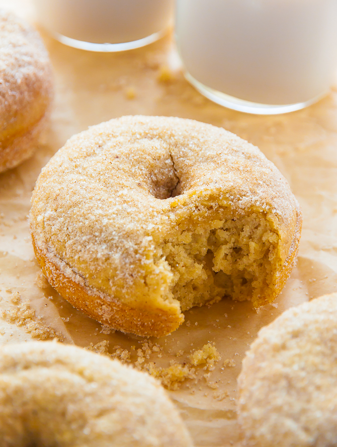 Baked cinnamon sugar donuts on parchment paper with a glass of milk.