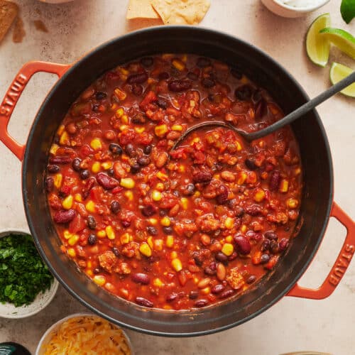 Pot of turkey chili with ladle in the pot and garnishes on the side.