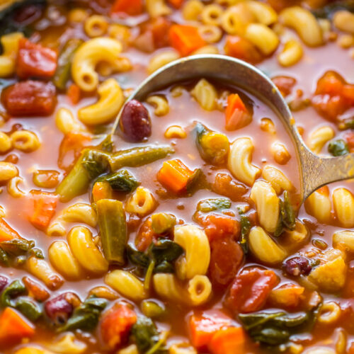 Minestrone soup being ladled out of a soup pot.