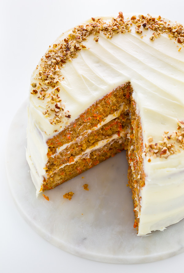 Whole carrot cake decorated with cream cheese frosting and nuts on a dessert plate.