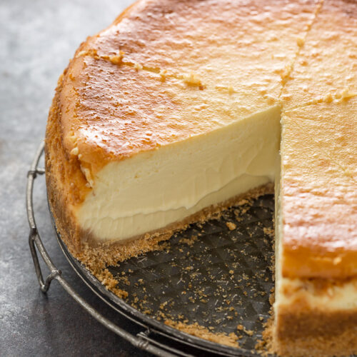 Thick style cheesecake on a spring form pan with a slice taken out.
