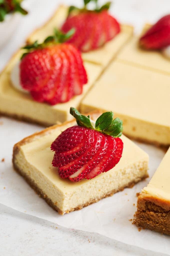 New York-Style Cheesecake Bars have a classic cheesecake filling and crunchy graham cracker crust! Full-fat cream cheese and sour cream are the secret to an ultra creamy cheesecake filling! Cut into squares and top with whipped cream and strawberries for a crowd-pleasing dessert everyone will love.