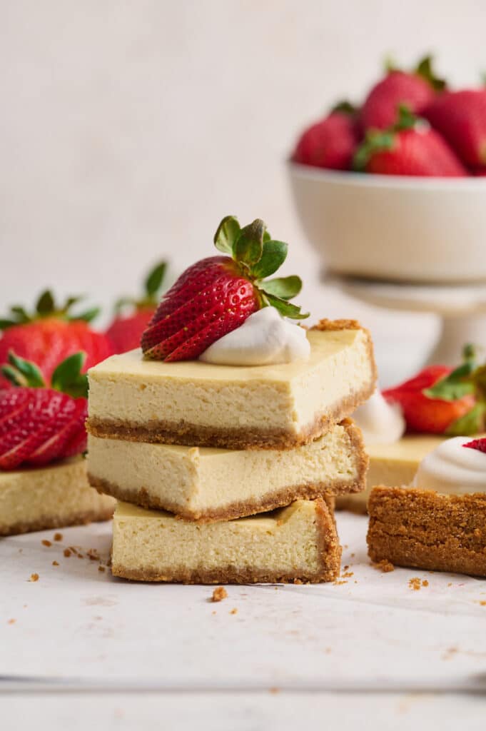 New York-Style Cheesecake Bars have a classic cheesecake filling and crunchy graham cracker crust! Full-fat cream cheese and sour cream are the secret to an ultra creamy cheesecake filling! Cut into squares and top with whipped cream and strawberries for a crowd-pleasing dessert everyone will love.