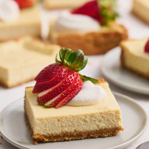 New York-Style Cheesecake Bars have a classic cheesecake filling and crunchy graham cracker crust! Full-fat cream cheese and sour cream are the secret to an ultra creamy cheesecake filling! Cut into squares and top with whipped cream and strawberries for a crowd-pleasing dessert everyone will love.