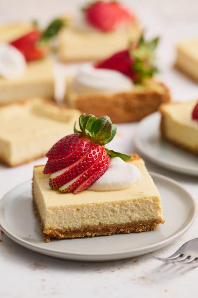 New York-Style Cheesecake Bars have a classic cheesecake filling and crunchy graham cracker crust! Full-fat cream cheese and sour cream are the secret to an ultra creamy cheesecake filling! Cut into squares and top with whipped cream and strawberries for a crowd-pleasing dessert everyone will love.