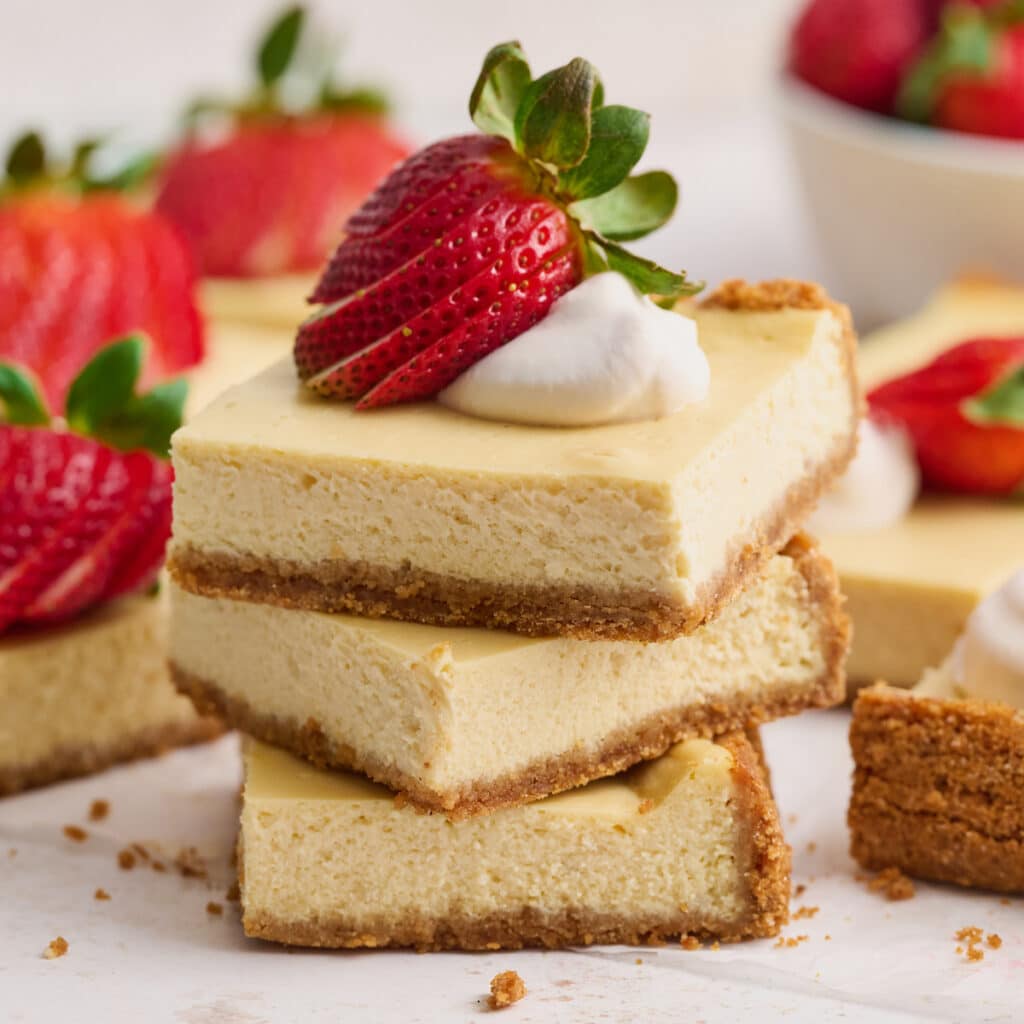 New York-Style Cheesecake Bars have a classic cheesecake filling and crunchy graham cracker crust! Full-fat cream cheese and sour cream are the secret to an ultra creamy cheesecake filling! Cut into squares and top with whipped cream and strawberries for a crowd-pleasing dessert everyone will love.