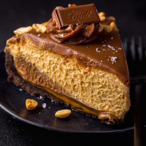 Slice of peanut butter pie on a black plate topped with chocolate ganache.