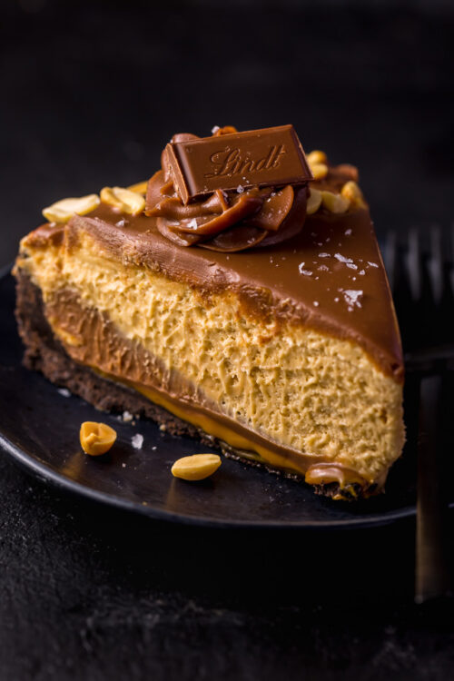 Slice of peanut butter pie on a black plate topped with chocolate ganache.