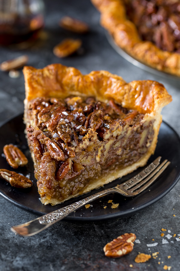 Slice of homemade pecan pie on a black plate with dessert fork.