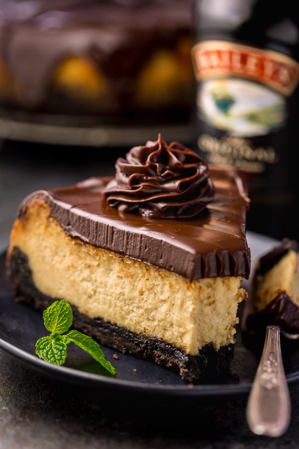 Slice of baileys cheesecake topped with chocolate ganache on a black plate.