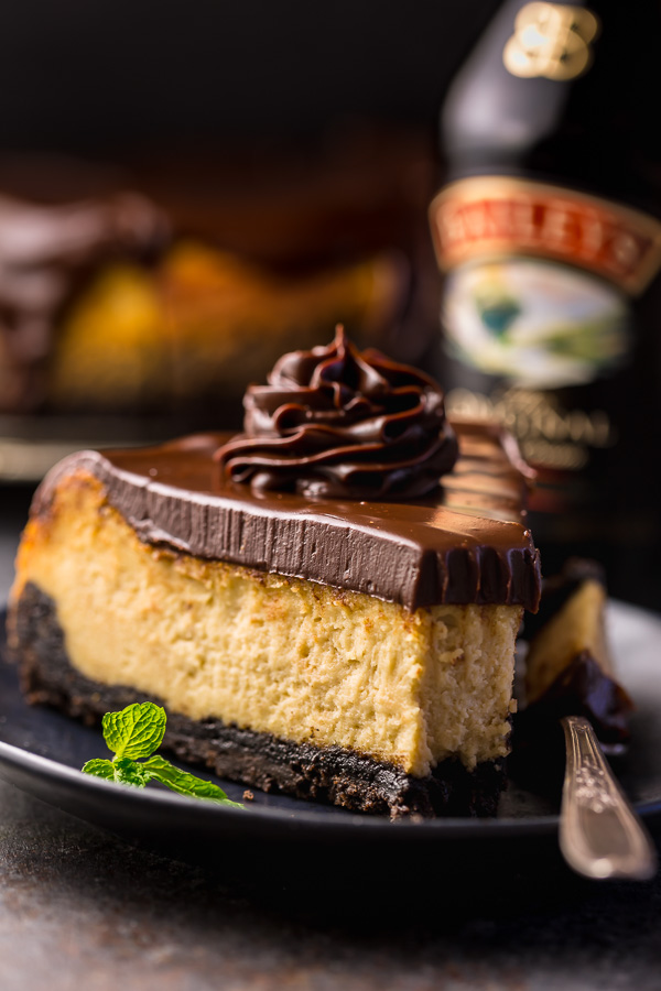 Slice of baileys cheesecake topped with chocolate ganache on a black plate.