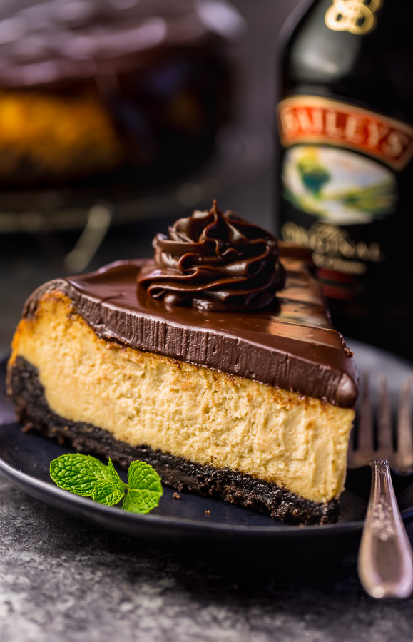 Slice of baileys cheesecake on a black plate with chocolate ganache on top.