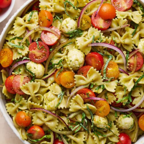 Big bowl of pasta salad with cherry tomatoes, red onion, and Italian dressing on top.