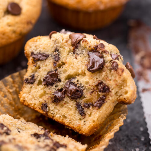 Chocolate chip muffin split in half in paper muffin liner.
