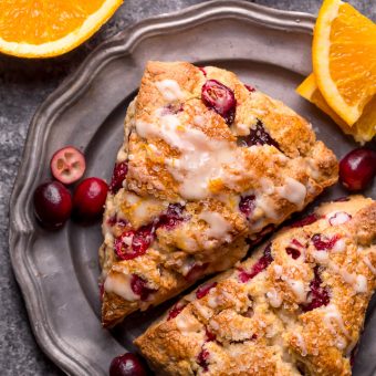 Cranberry orange scones on a plate with cranberries and oranges around it.