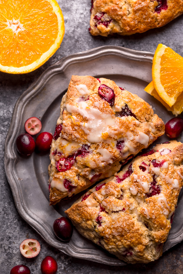 Cranberry orange scones on a plate with cranberries and oranges around it.