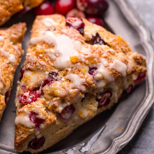Cranberry orange scone on a plate with orange glaze on top.
