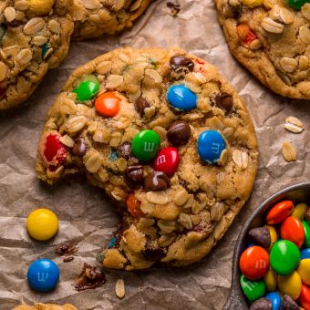 Monster cookies on a baking sheet with chocolate chips and chocolate candy.