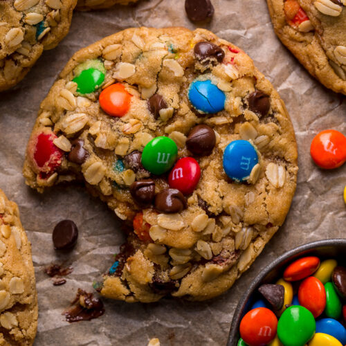 Monster cookies on baking sheet with a bite taken out.