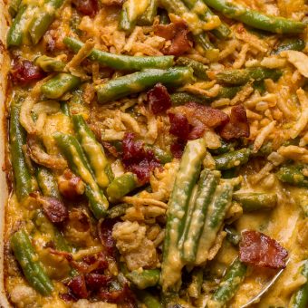Baking dish with green bean casserole covered in a cheesy bacon sauce with a serving spoon.