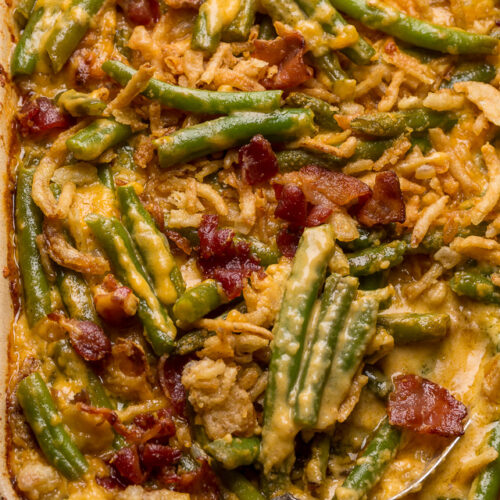 Baking dish with green bean casserole covered in a cheesy bacon sauce with a serving spoon.