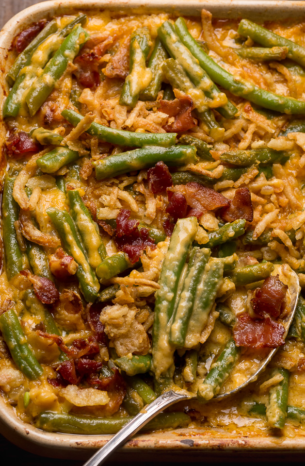 Baking dish with green bean casserole covered in a cheesy bacon sauce with a serving spoon.