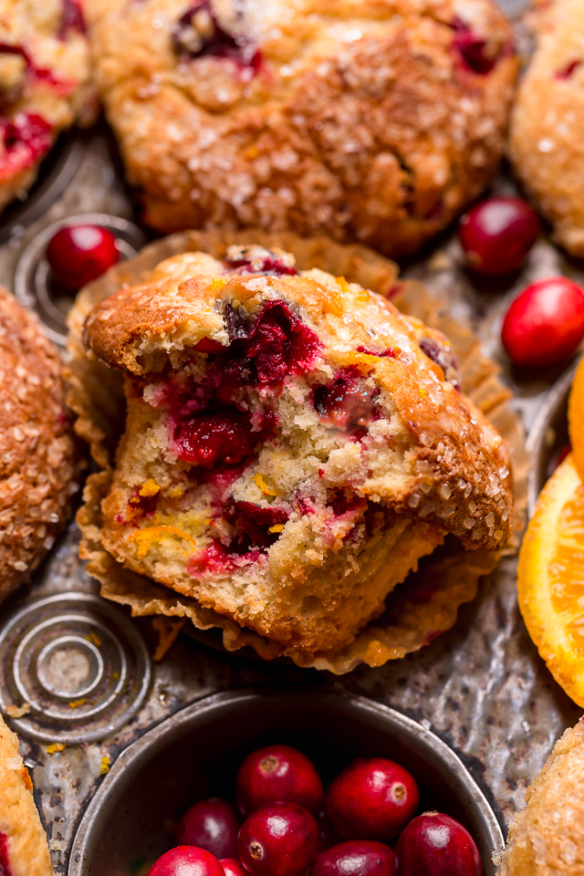 Cranberry orange muffins in a muffin pan surrounded by fresh cranberries.