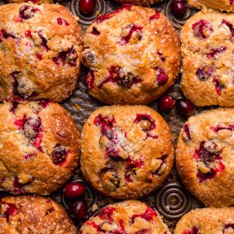 Cranberry orange muffins in a muffin pan with fresh cranberries and orange zest on top.